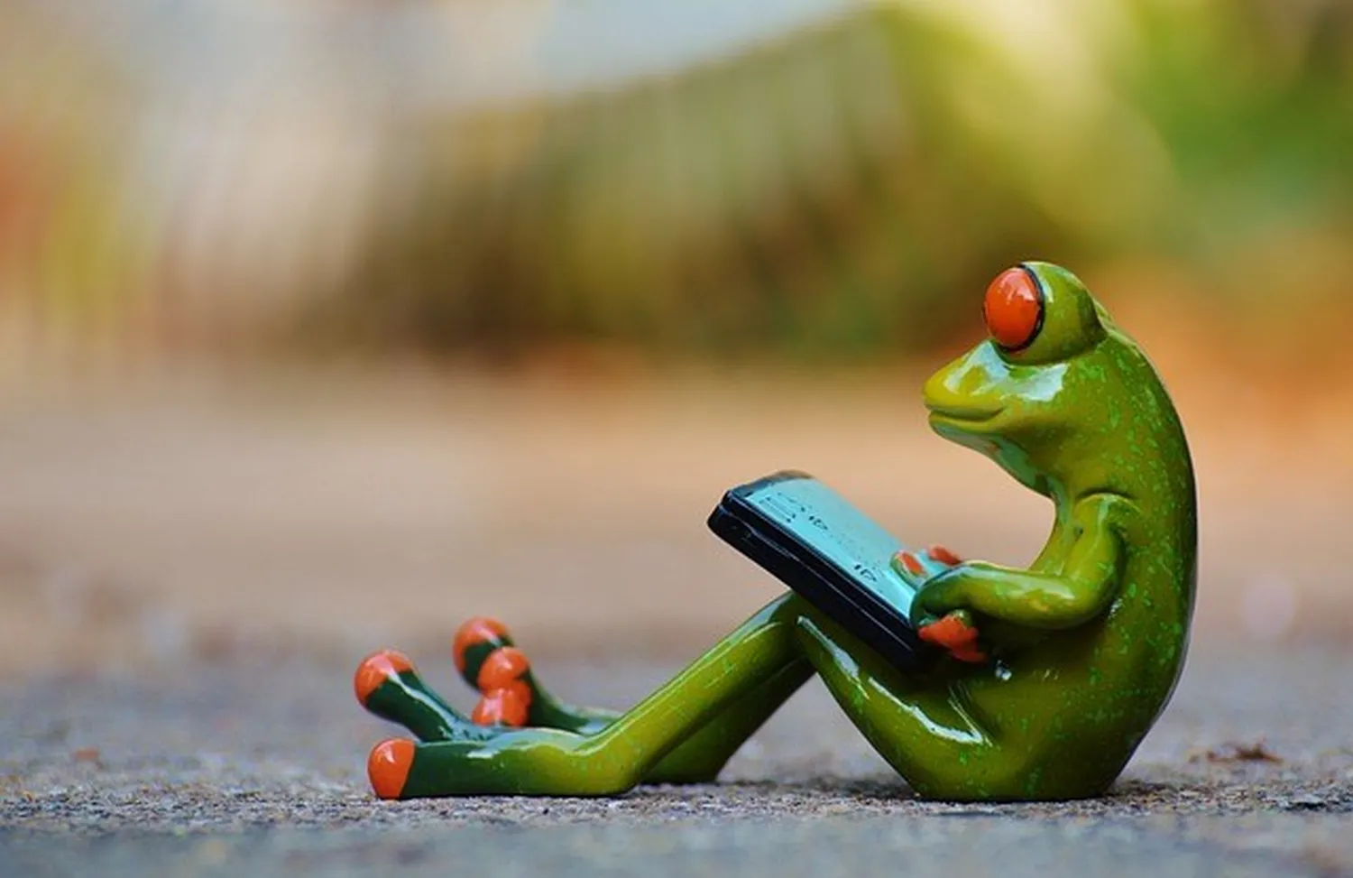 enHealing - Energetischen Praxis, persönlichen Entwicklung und Vitalstoffberatung - Eine grüne Froschfigur sitzt da und schaut auf ein Smartphone.