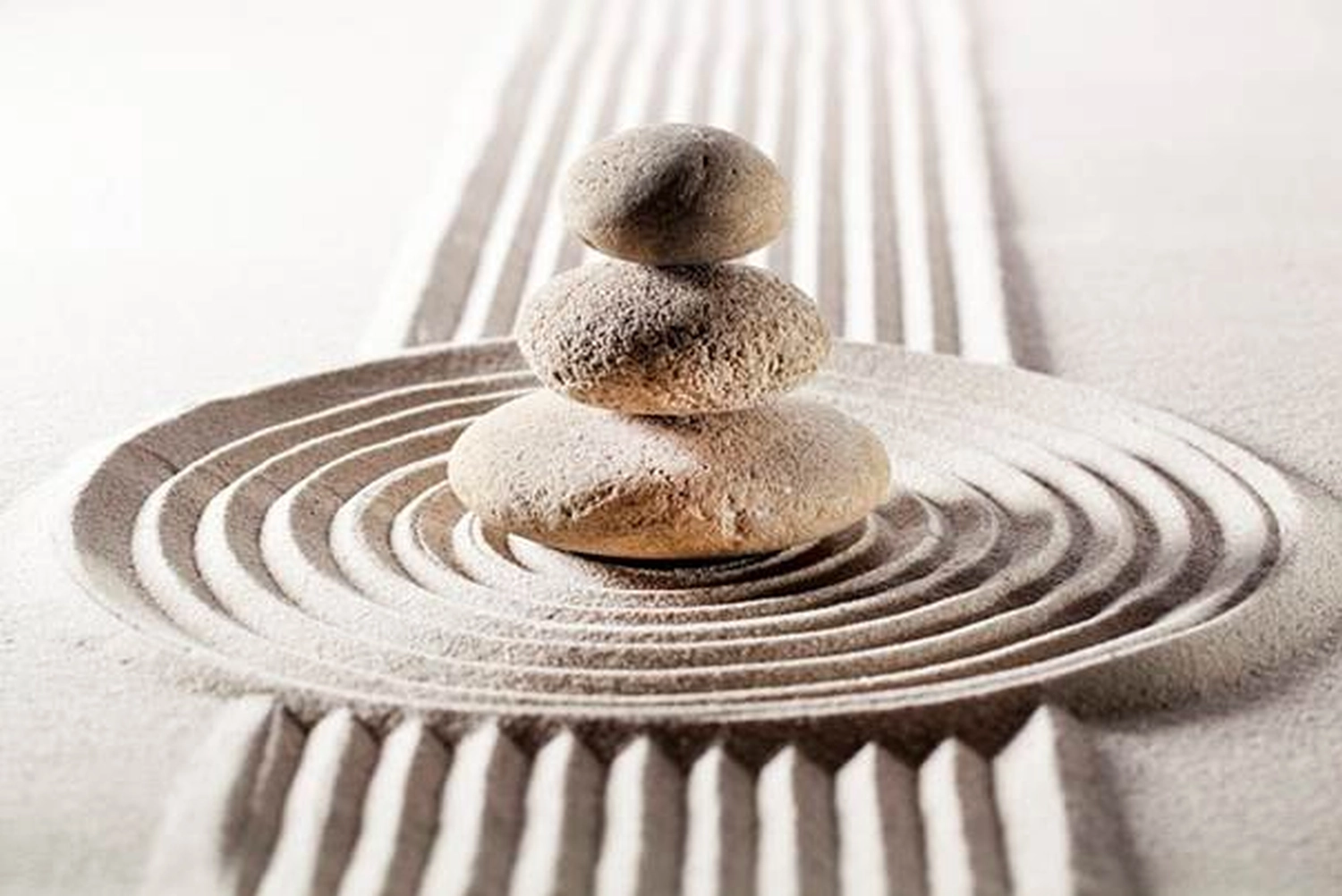 enHealing - Energetischen Praxis, persönlichen Entwicklung und Vitalstoffberatung - In der Mitte eines kreisförmigen, in den Sand geharkten Musters befindet sich ein Stapel aus drei ausbalancierten Steinen, flankiert von geraden, parallelen, geharkten Linien.